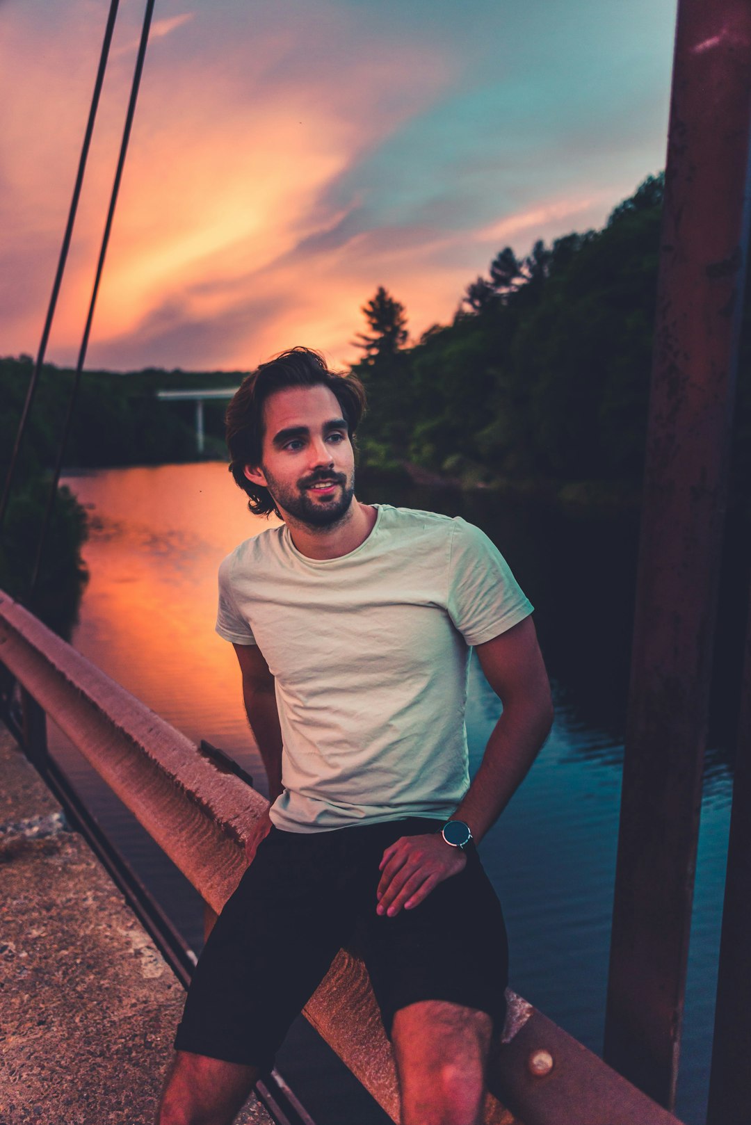 man in white crew neck t-shirt and black shorts standing on brown wooden bridge during