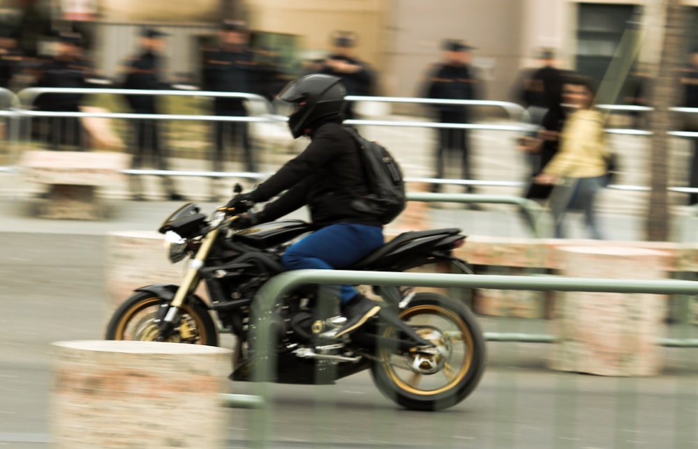 Mann in schwarzer Jacke und blauer Jeans fährt schwarzes Motorrad