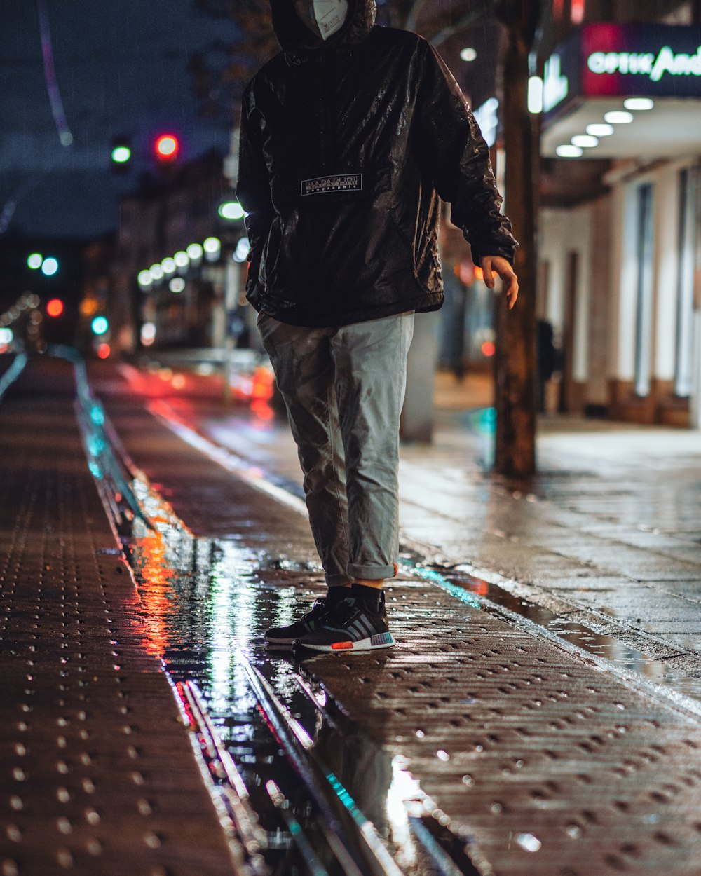 Hombre con chaqueta negra y pantalones grises caminando por la calle durante la noche