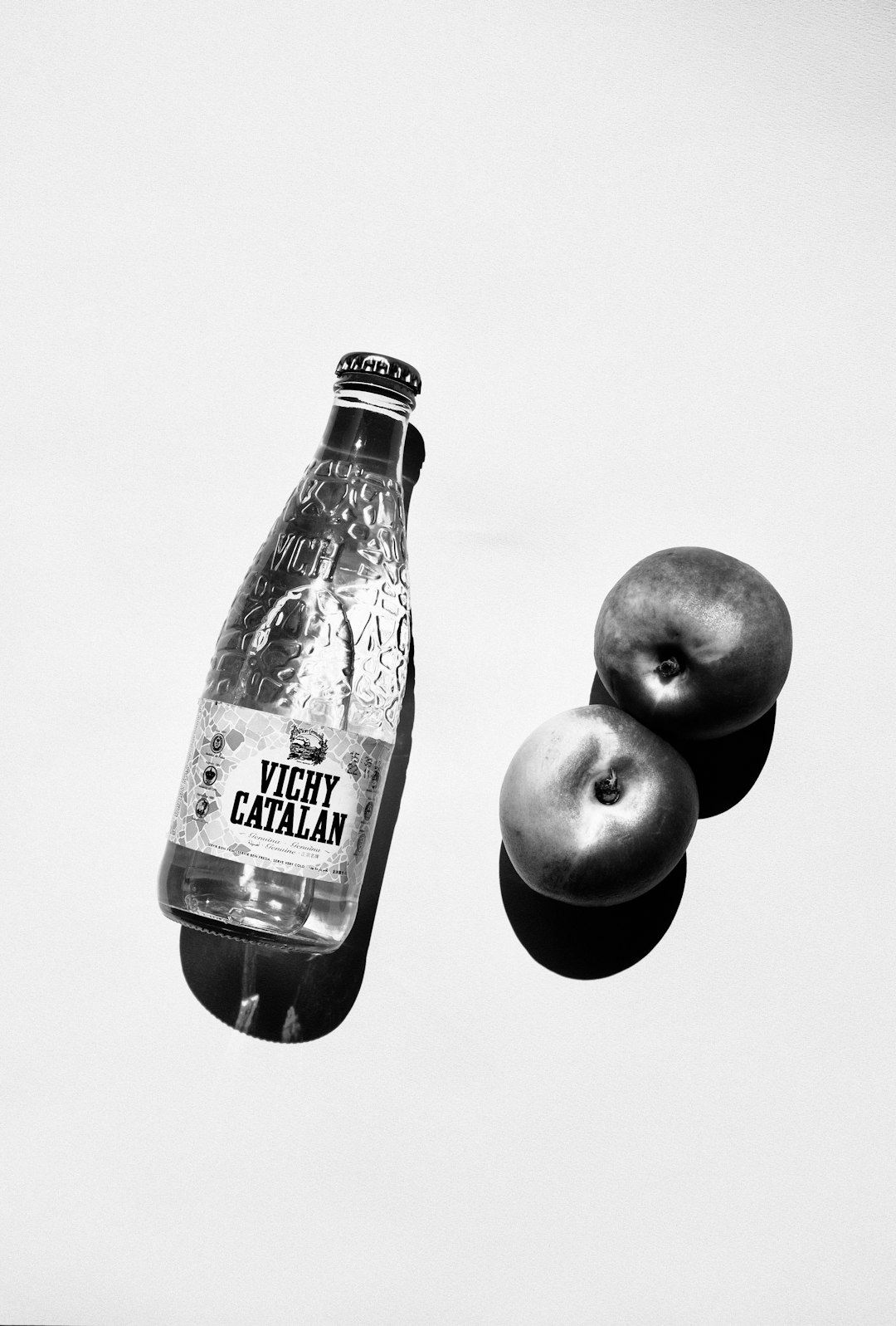 grayscale photo of green apple beside clear glass bottle
