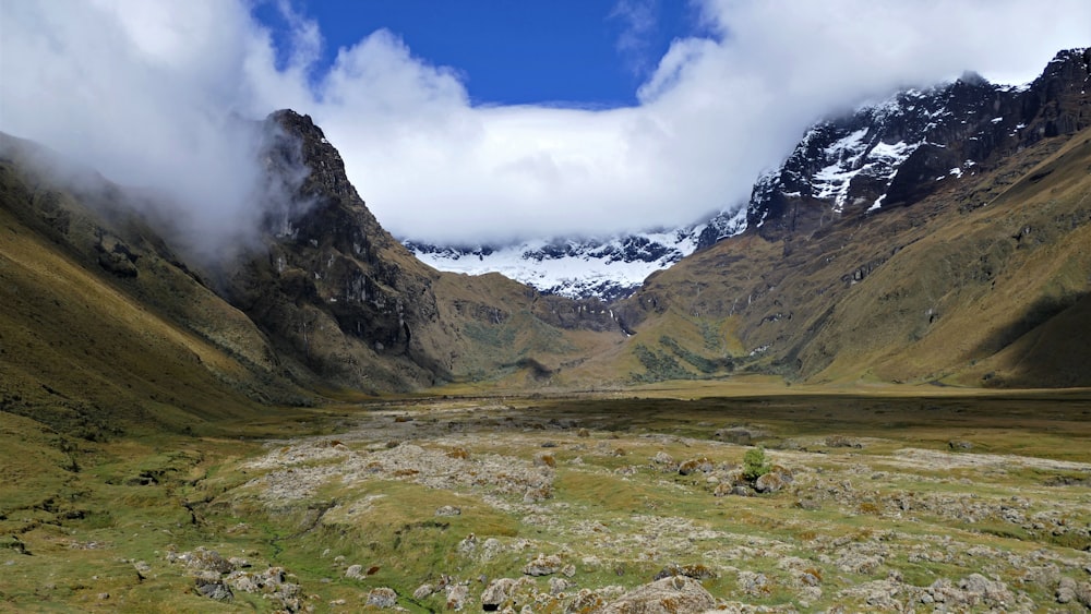 green grass field near mountain under white clouds and blue sky during daytime