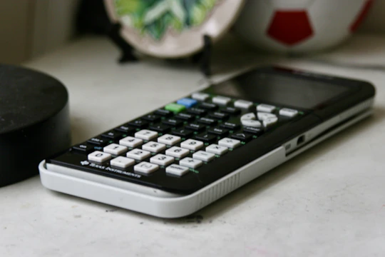 A sleek digital pocket calculator with bright buttons on a wooden desk.