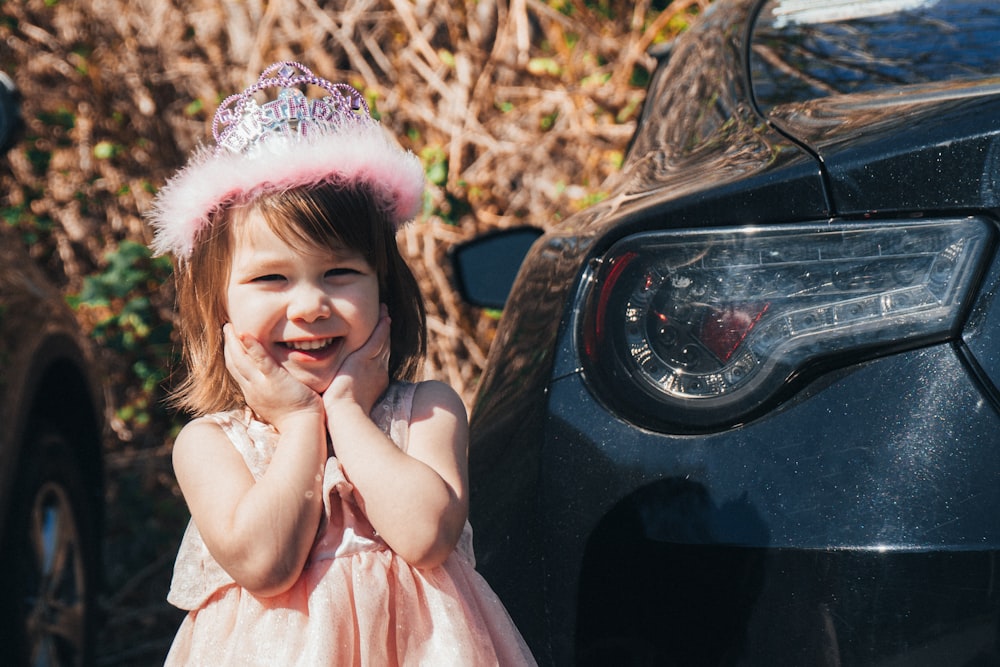 ragazza in vestito rosa che si siede sull'automobile nera