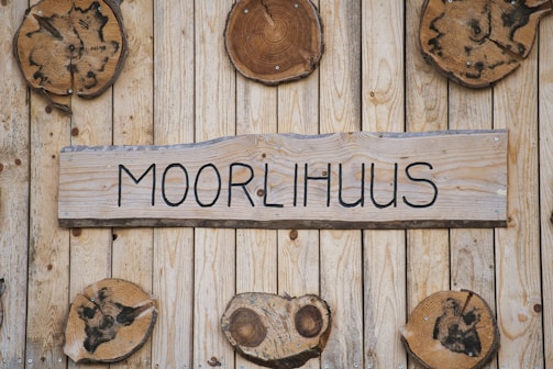 A wooden wall with several round, wooden slices attached, featuring unique dark patterns. In the center, there is a rectangular wooden plaque with the word 'MOORLIHUUS' written in a bold, black font.
