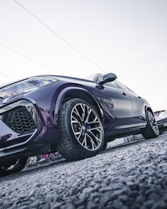 Side angle of a black SUV with shiny rims on a gravel road.