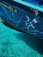 Close-up of the polished turquoise hull reflecting sunlight on calm canal waters.