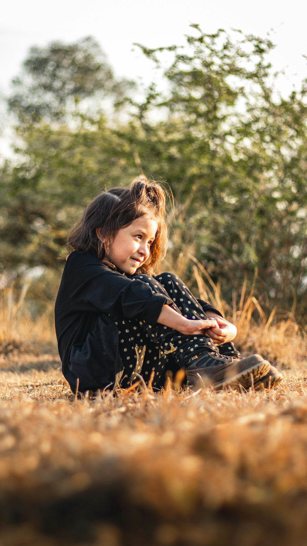 girl in black long sleeve shirt sitting on brown grass field during daytime