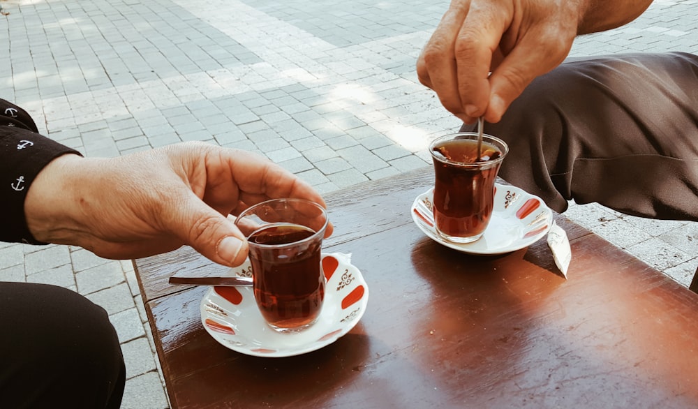 personne tenant une tasse en verre transparent avec un liquide brun