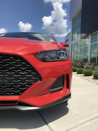 A shiny red car parked in front of a modern building under clear skies.