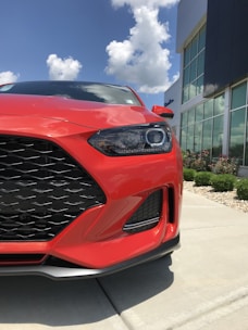 A shiny red car parked in front of a modern building under clear skies.