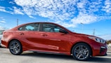 A red compact hatchback gleaming under a clear blue sky in an open lot.