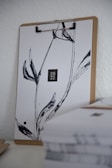 A clipboard is holding a sheet of paper with minimalist black ink design resembling plant stems. The paper prominently displays '2022' in the center. In the foreground, there is a stack of papers that is slightly out of focus.