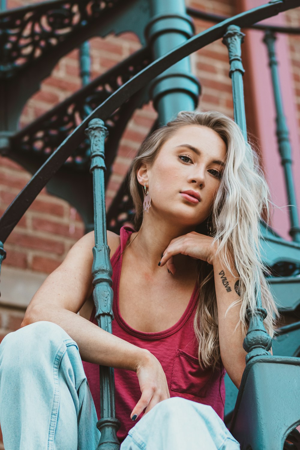 woman in red tank top and blue denim jeans sitting on metal bar during daytime