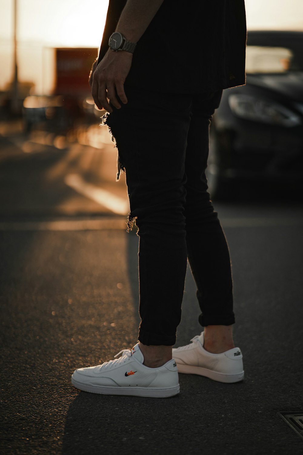 person in black pants and white nike sneakers standing on road during daytime