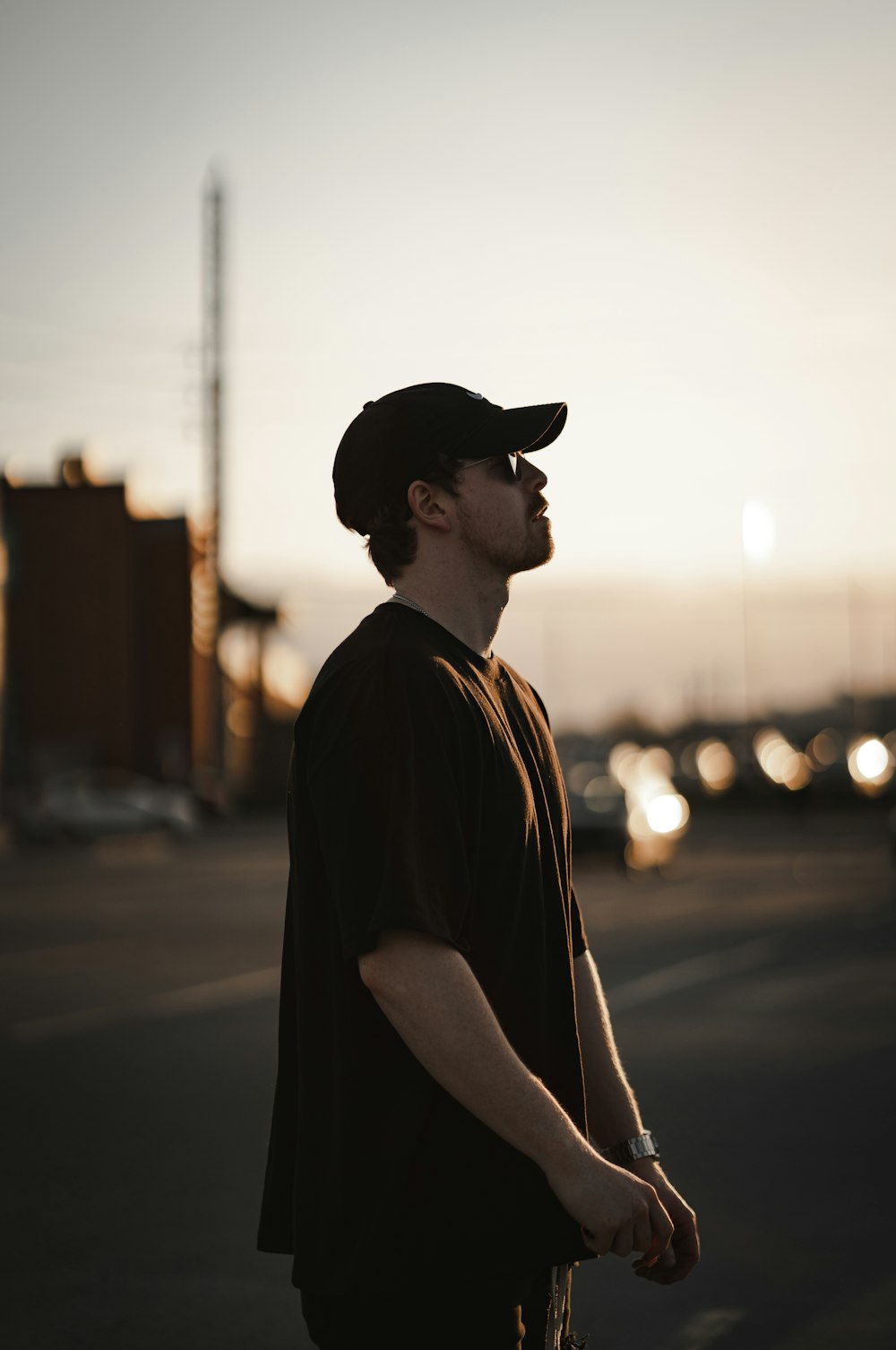 man in black shirt and black hat standing on sidewalk during sunset