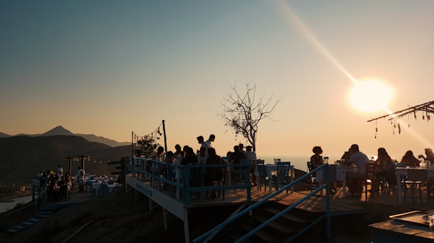 A cozy mountain terrace at sunset with warm orange lights and dark wooden furniture.