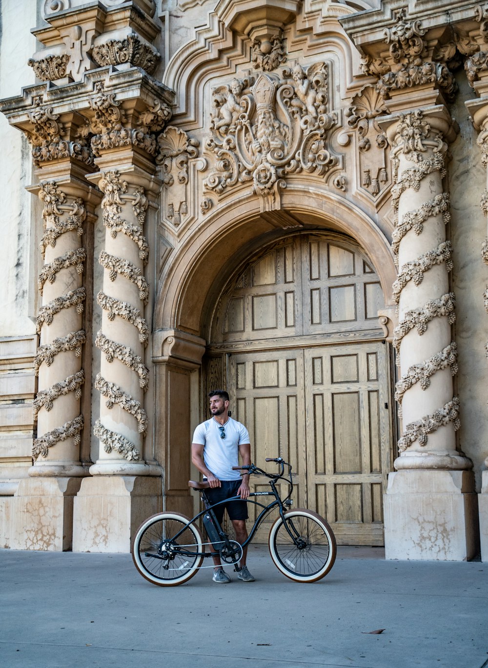 uomo in camicia bianca in bicicletta vicino a un edificio in cemento marrone durante il giorno