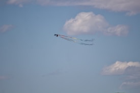 A colorful kite with a long tail streaming in the sky, surrounded by fluffy white clouds on a clear blue day.