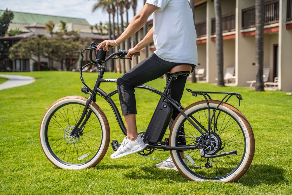 man in white t-shirt and black pants riding black bicycle on green grass field during