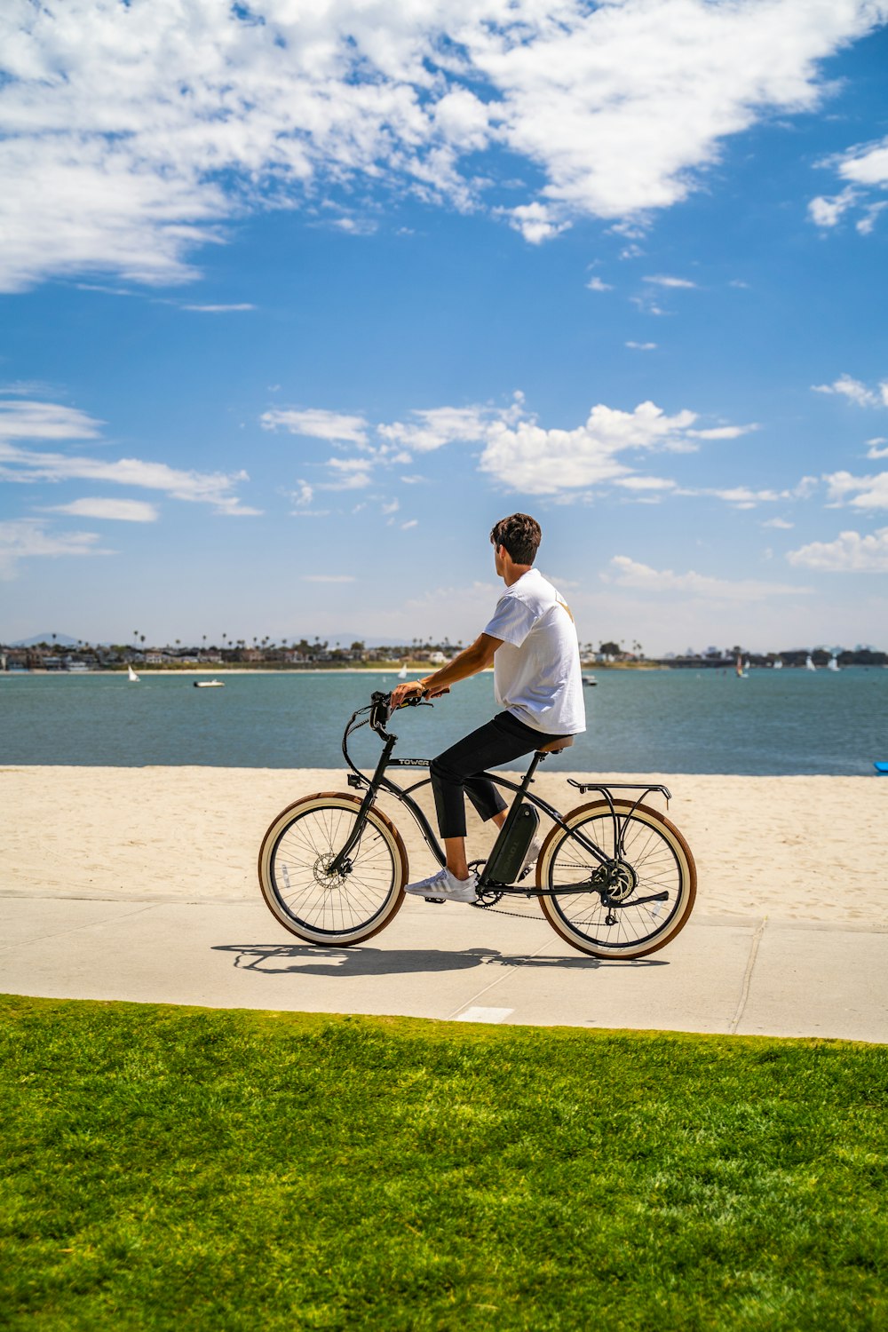 낮 동안 바다 근처에서 검은 자전거를 타고 있는 흰색 드레스 셔츠를 입은 남자