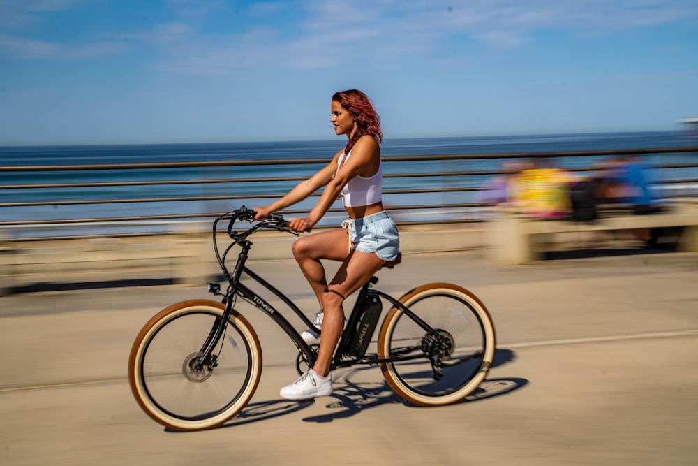 woman in white bikini riding on black bicycle on road during daytime