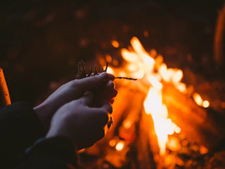 Hands holding a glowing fire starter ready to light a campfire.