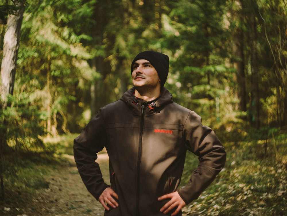 man in black zip up jacket standing in forest during daytime