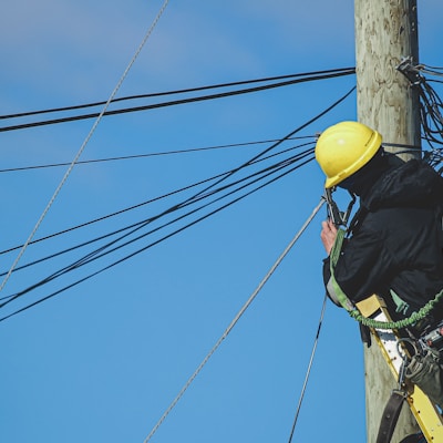 man in black jacket and yellow hard hat climbing on brown wooden post during daytime