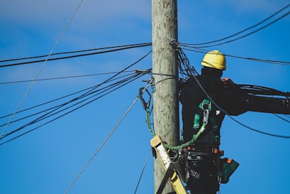 man in black jacket and yellow helmet on brown wooden post under blue sky during daytime
