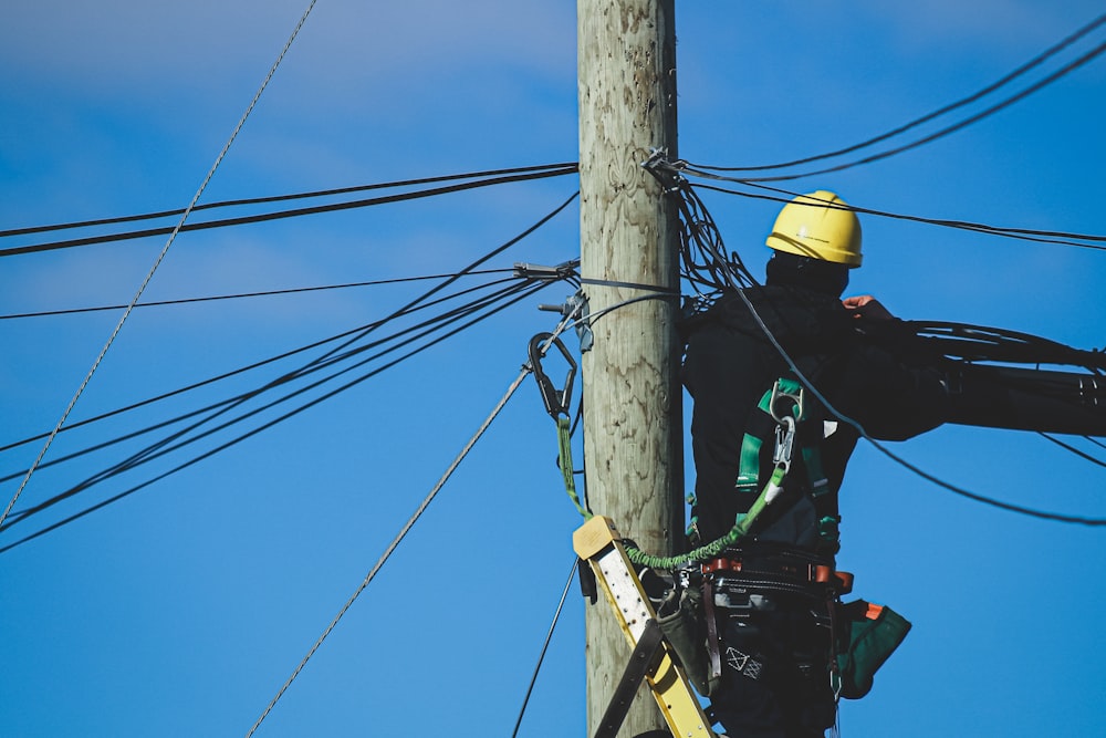 man in black jacket and yellow helmet on brown wooden post under blue sky during daytime