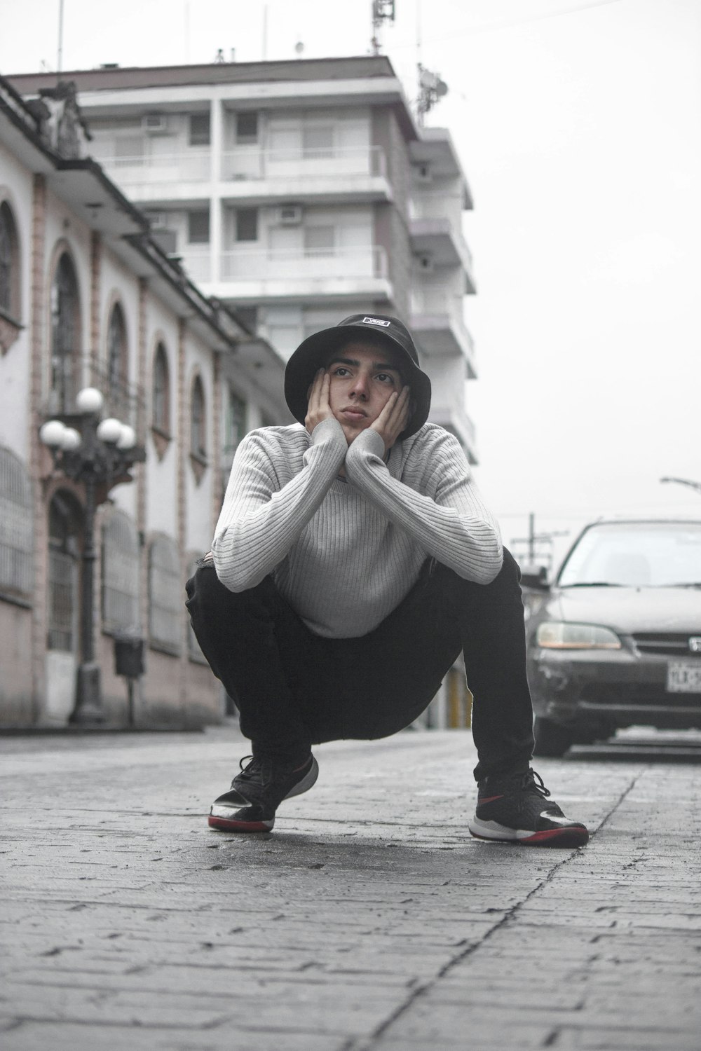 woman in gray sweater and black pants sitting on gray concrete pavement during daytime