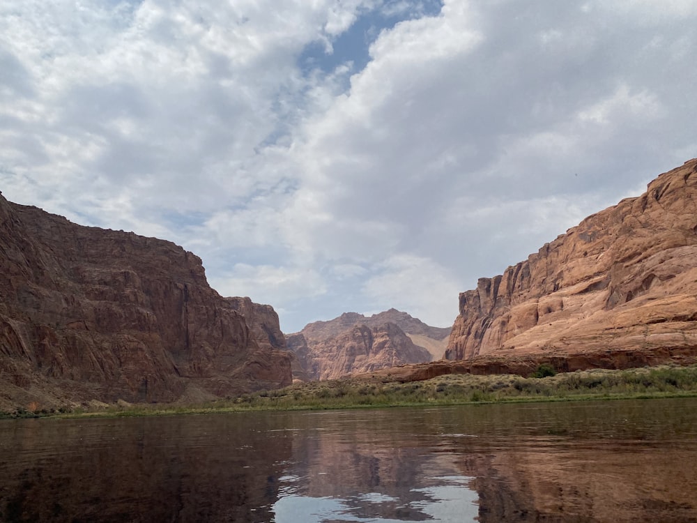 brown rocky mountain beside lake under white clouds during daytime