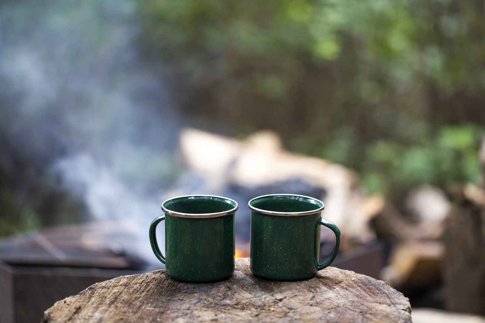 Two green mugs on a log at a woodland campsite