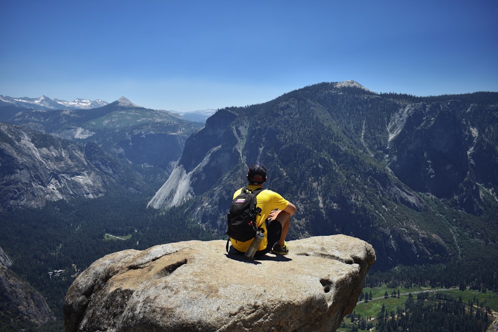man in yellow shirt sitting on rock mountain during daytime