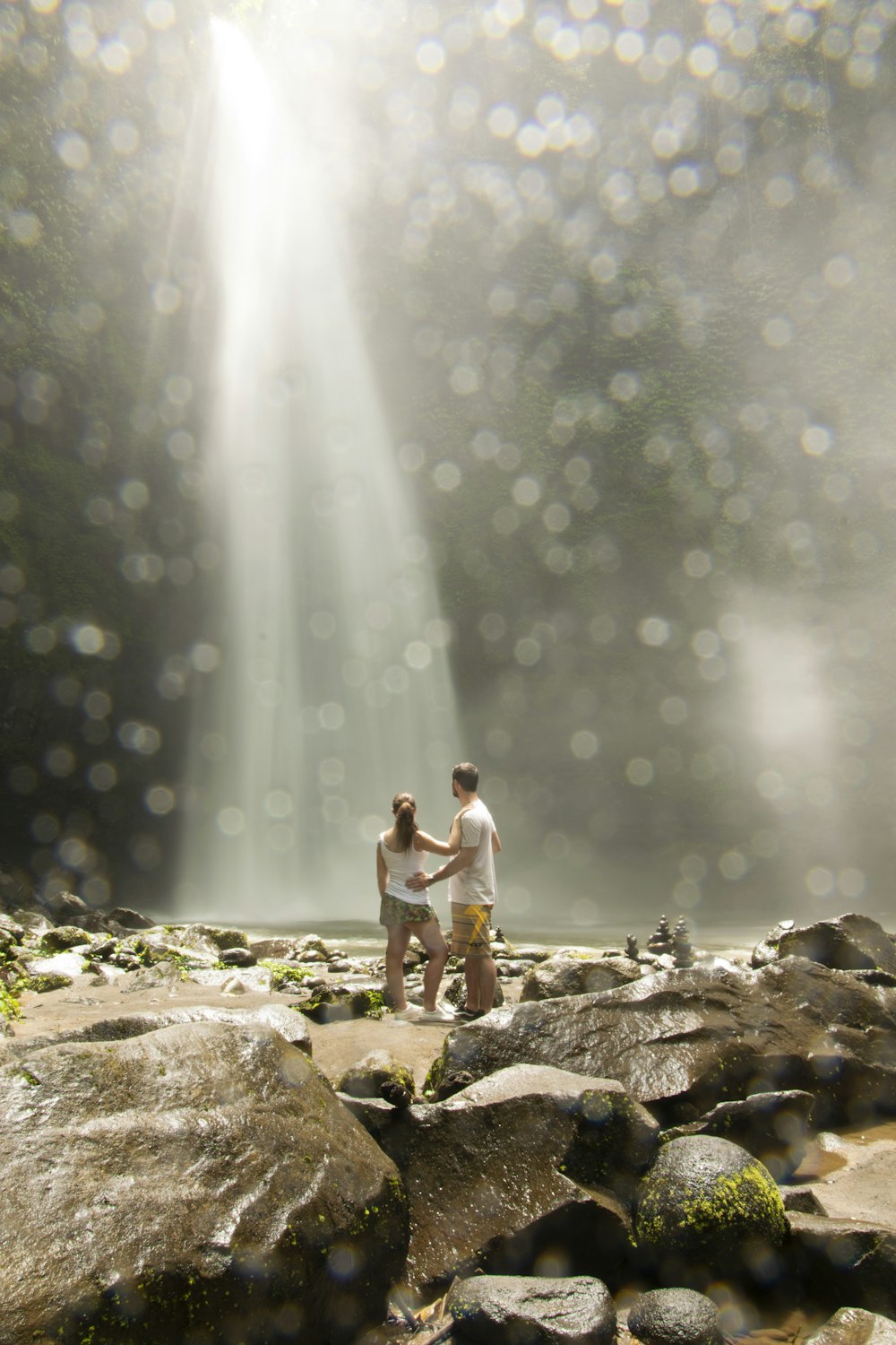 2 women standing on rock near water falls during daytime