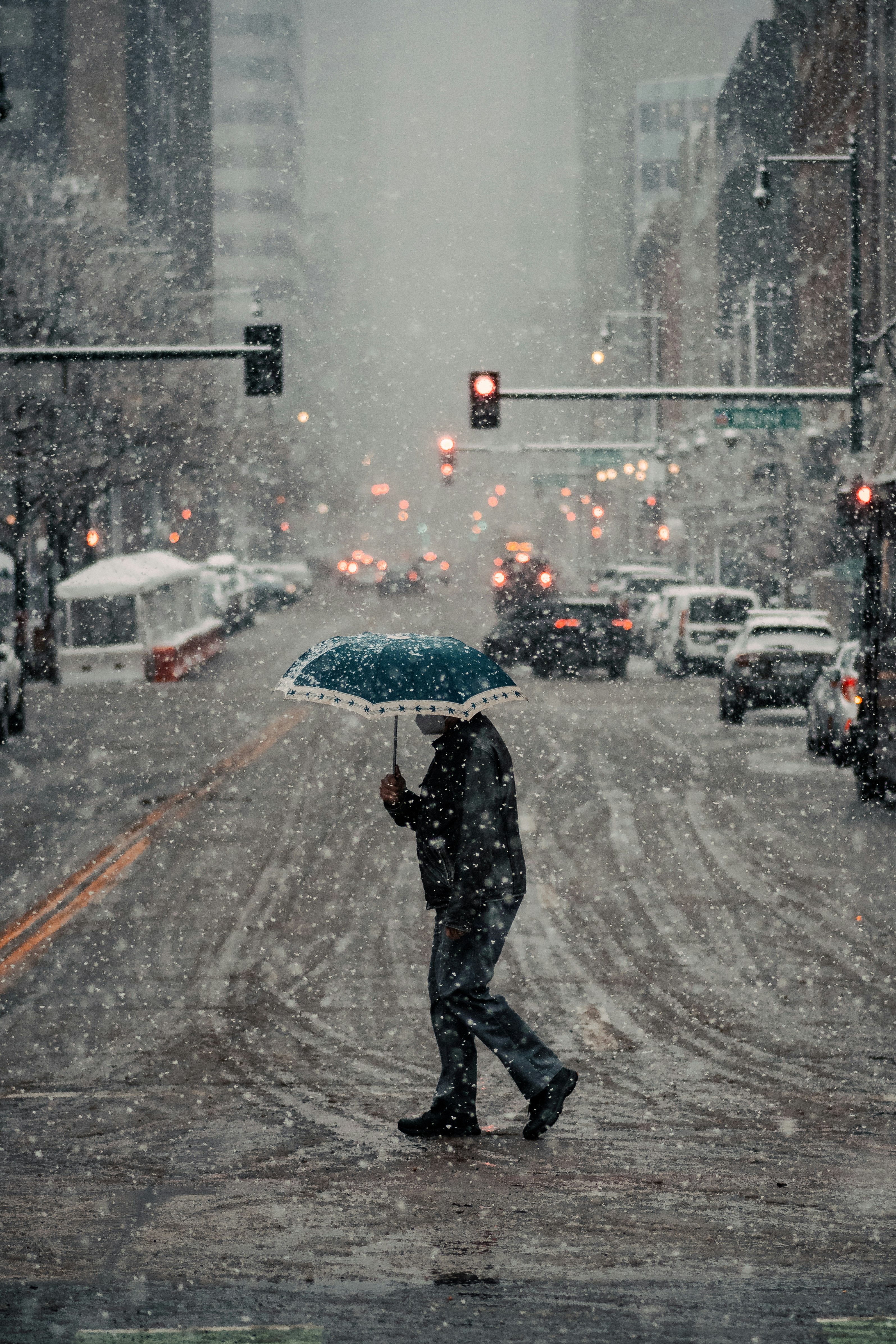 man in black jacket and pants holding umbrella walking on street during daytime