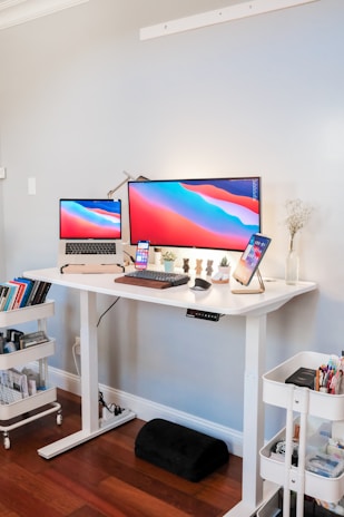 A modern standing desk converter holding a laptop and a notebook in a bright home office.
