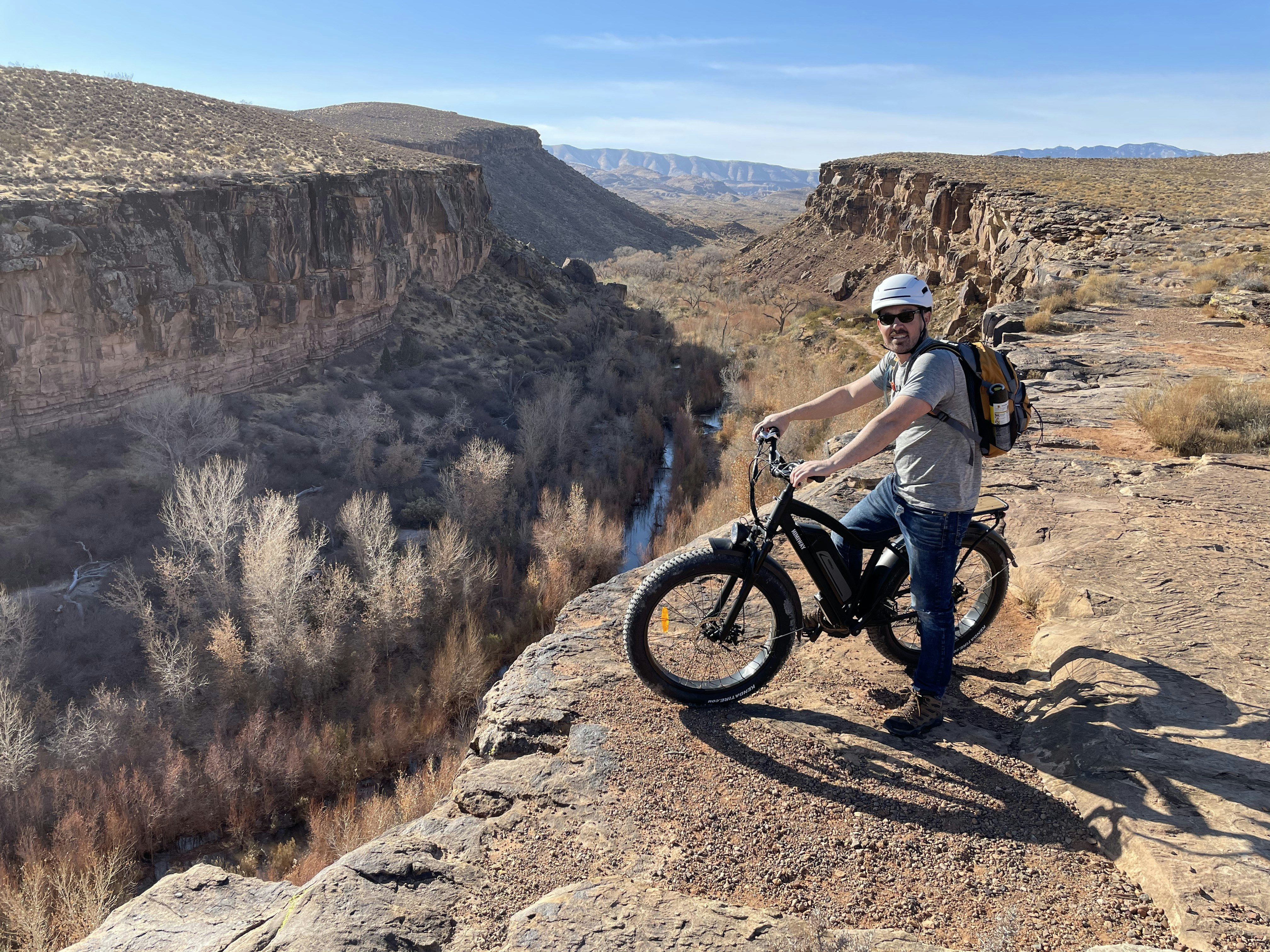 man in white shirt riding on black mountain bike on brown rocky mountain during daytime, Himiway ebike is able to ride up a steep hill and give you more fun of your cycling adventure.