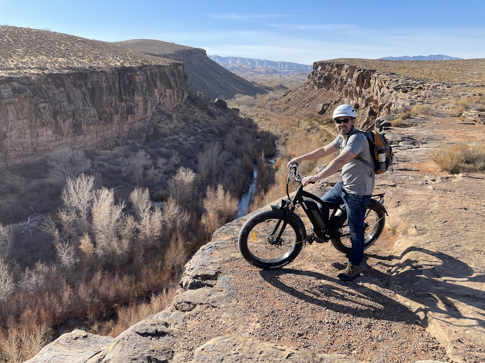 man in white shirt riding on black mountain bike on brown rocky mountain during daytime