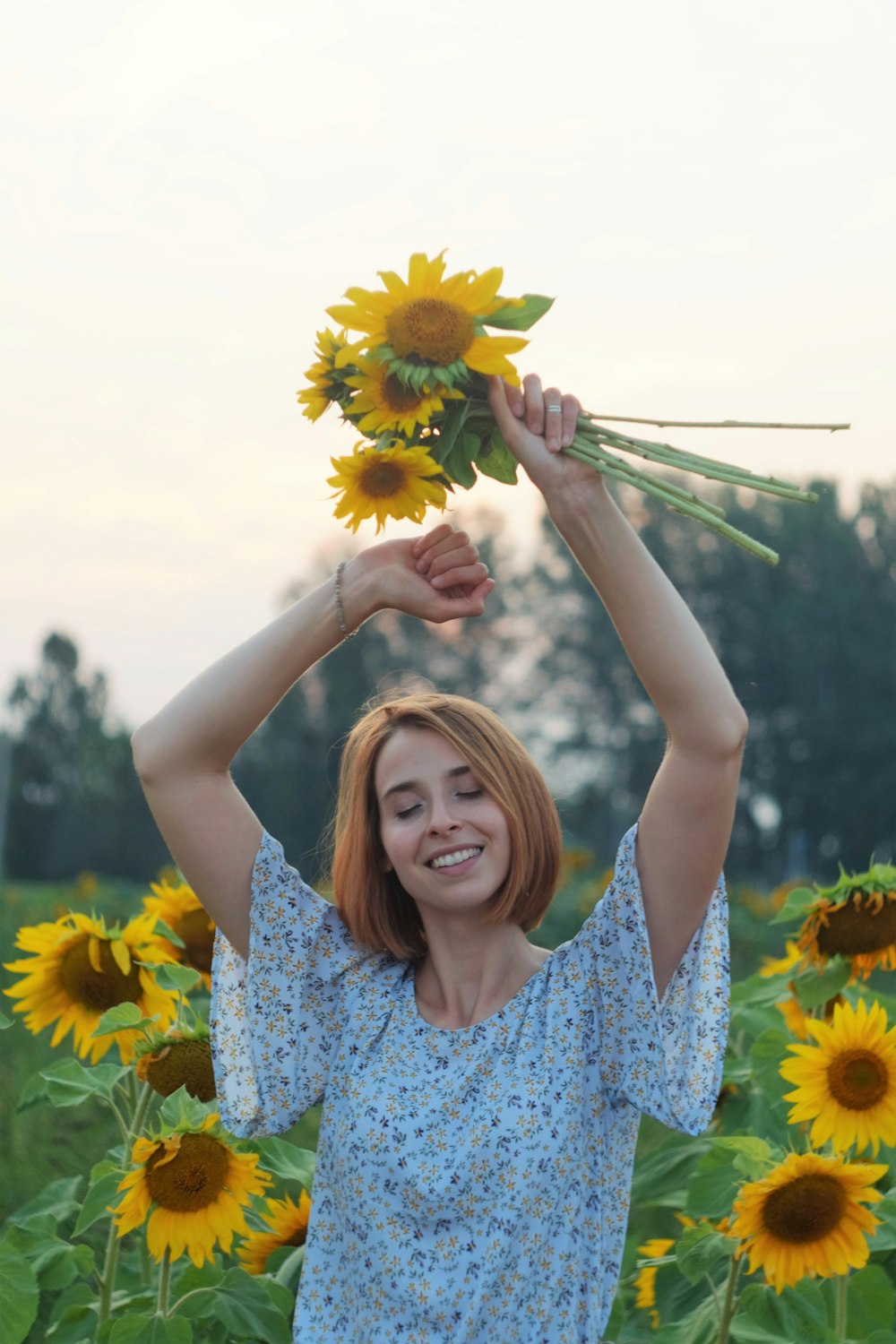 woman in blue and white floral dress holding sunflower during daytime