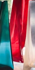 Glossy and translucent vase-like structures with smooth surfaces in rich colors, including teal, red, and a silvery hue. These forms stand close together, showcasing a sleek modern design.