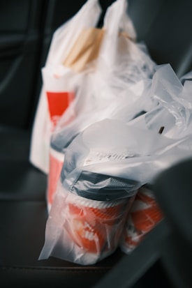 Several plastic grocery bags are placed on a car seat, containing takeout food containers.