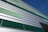 A modern building facade featuring horizontal metal panels in varying shades of green and silver. The design is geometric, with a pattern that alternates in color, giving a contemporary architectural appearance. The clear blue sky enhances the crisp lines and colors of the structure.