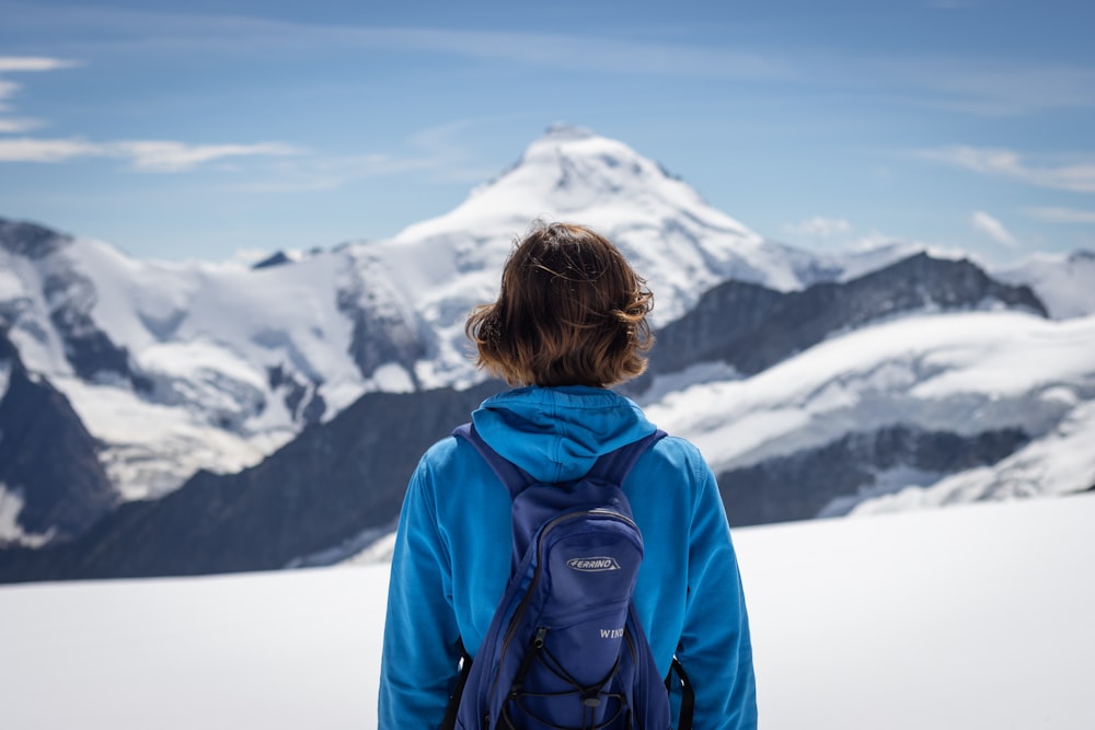 woman in blue jacket looking at snow covered mountain during daytime