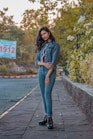 woman in gray hoodie and blue denim jeans standing on wooden dock during daytime