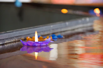 A softly glowing purple candle flickers against a deep black background, surrounded by delicate dried lavender and small crystals.