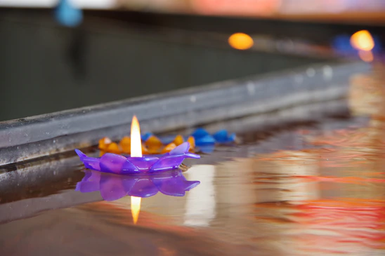 A softly glowing purple candle flickers against a deep black background, surrounded by delicate dried lavender and small crystals.