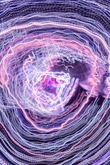 A swirling pattern of intricate light trails in various colors, primarily composed of blues, purples, and pinks. The lines create a vortex-like appearance, giving a sense of dynamic movement and energy.
