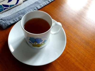 A warm ceramic cup of herbal tea resting on a wooden table beside a cream linen napkin.