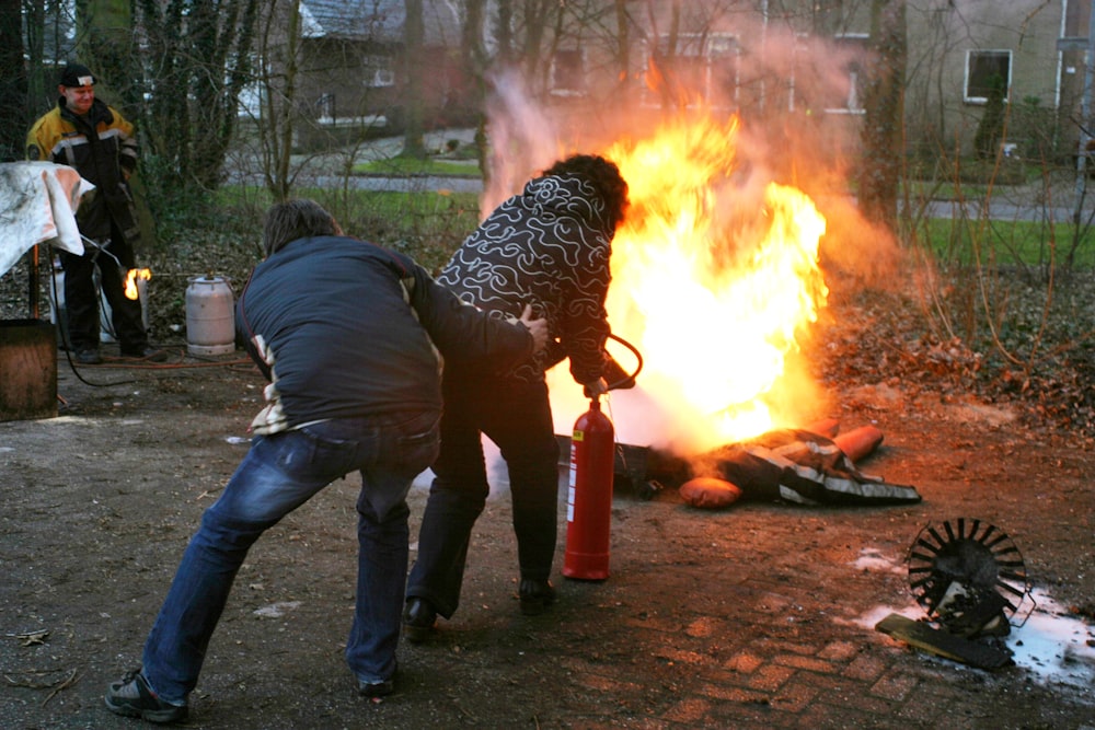 man in black jacket and blue denim jeans holding orange fire